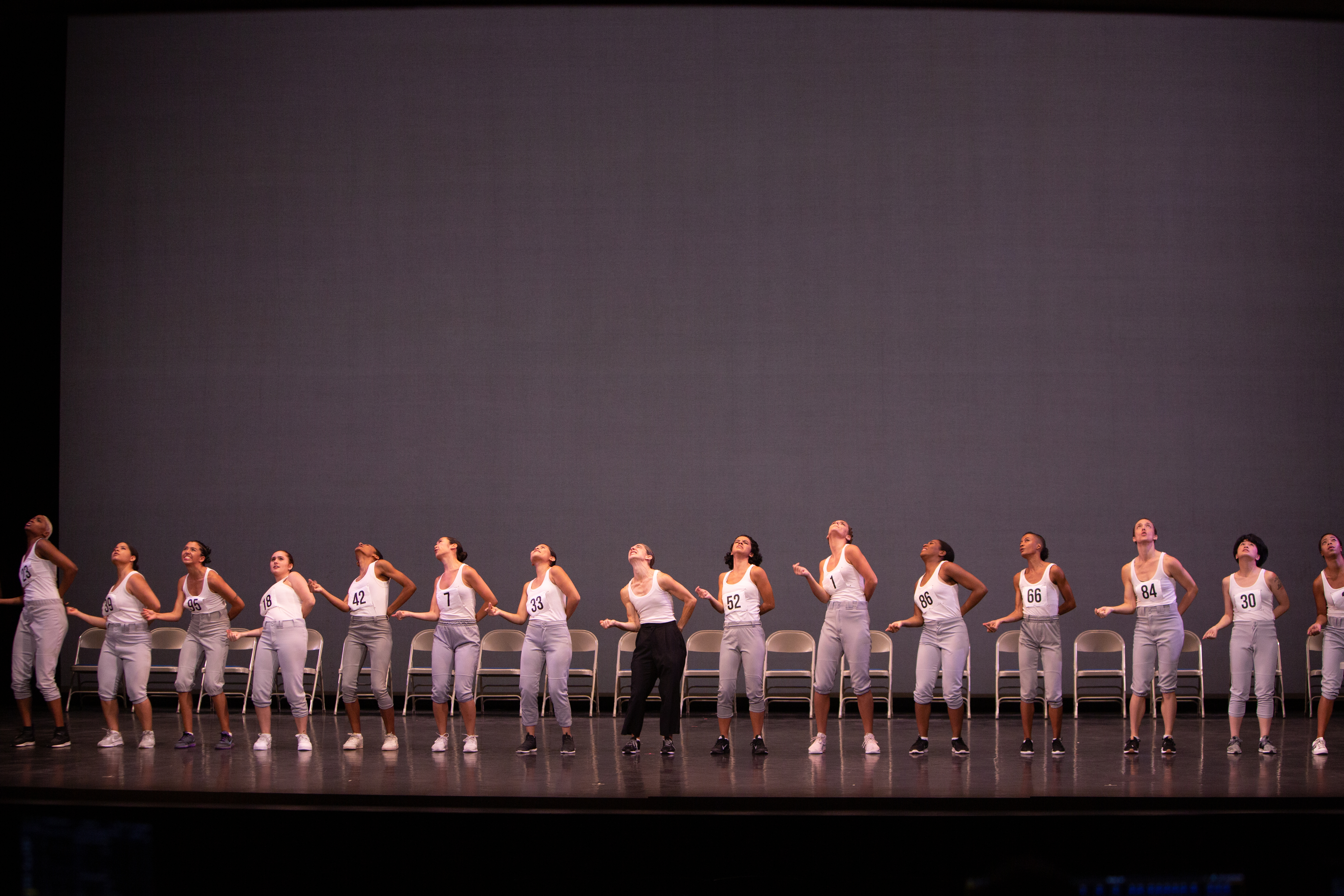 many dancers stand in a line in front of a line of chairs