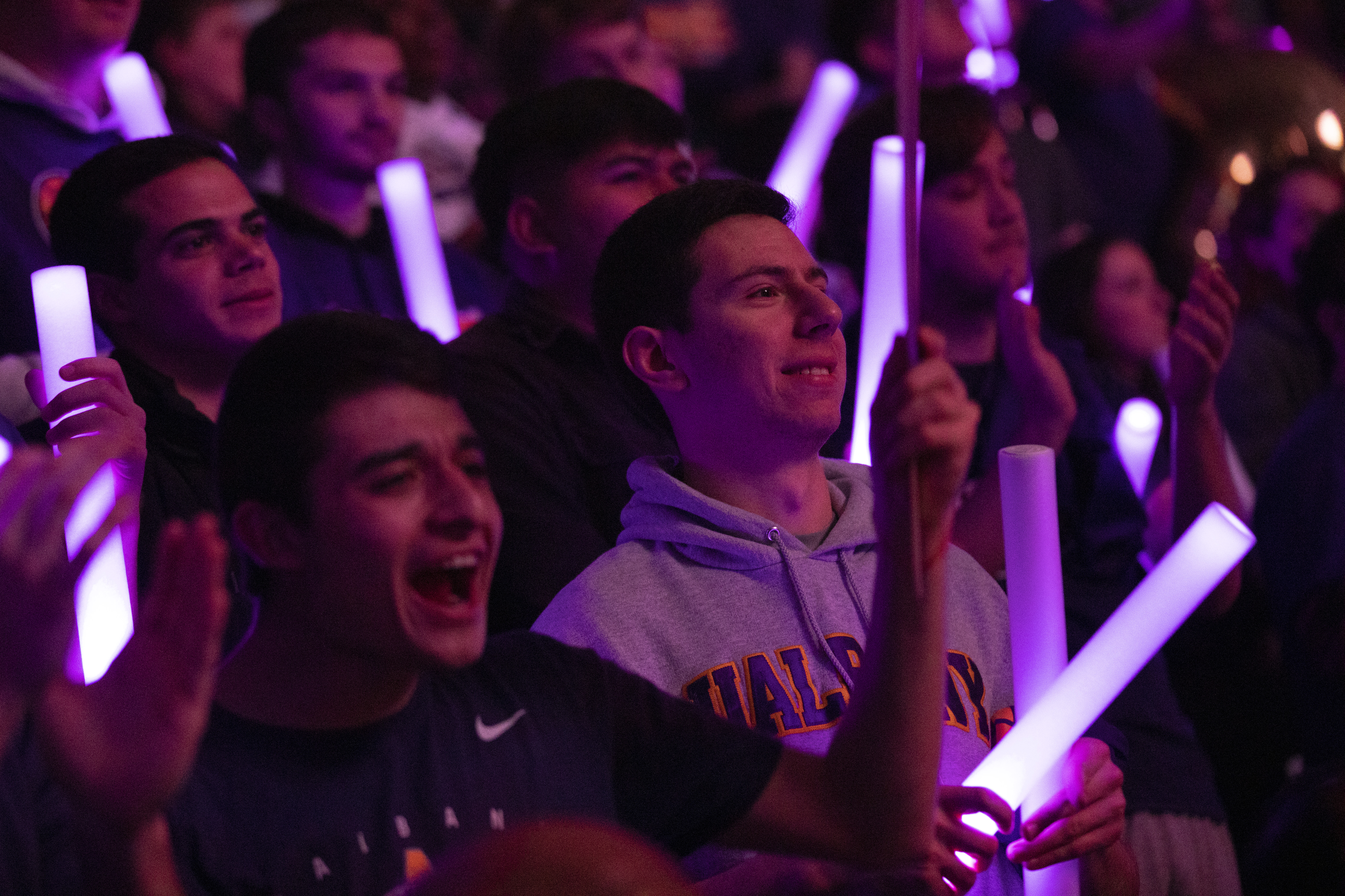 Students hold purple glow sticks as they stand and cheer for a UAlbany team