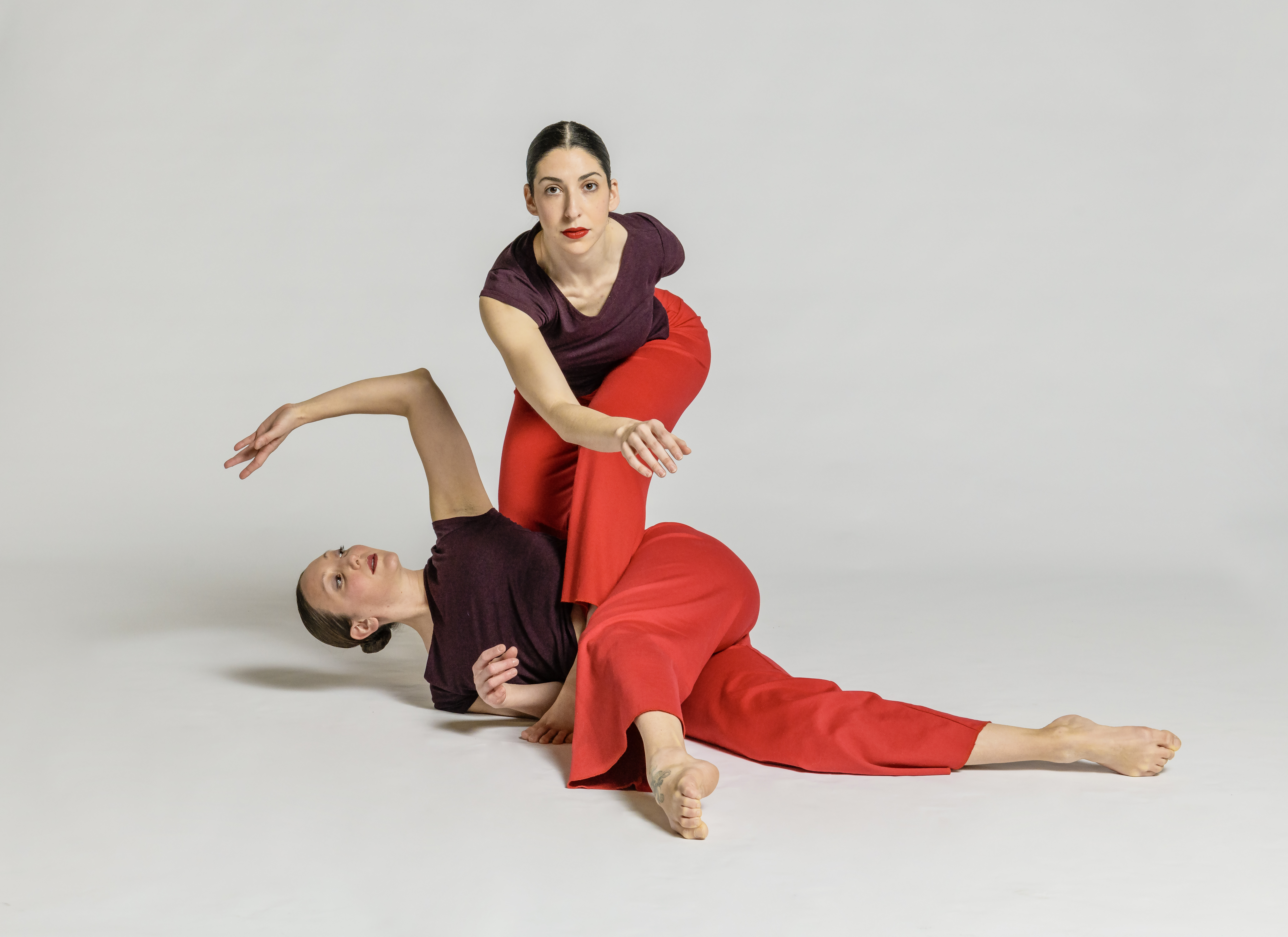 two dancers in red are intertwined wit one standing and the other on the floor