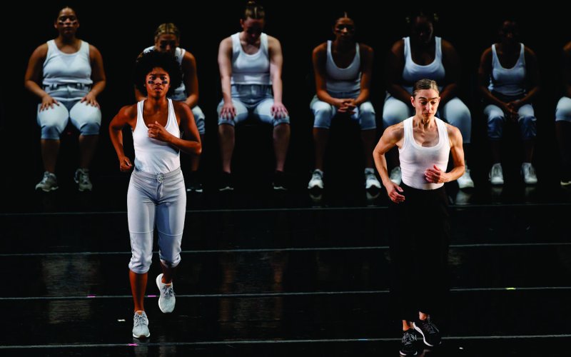 two dancers appear to be jogging in front of a line of dancers seated behind them