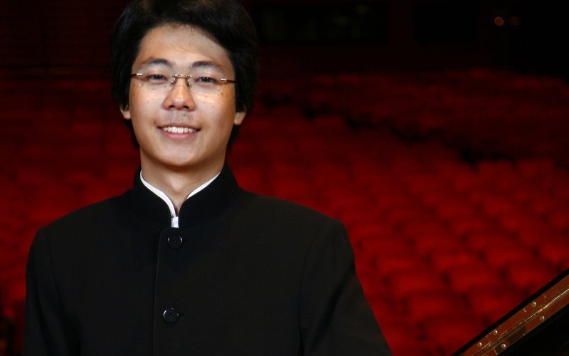 smiling individual with glasses dressed in black in front of red theatre seats