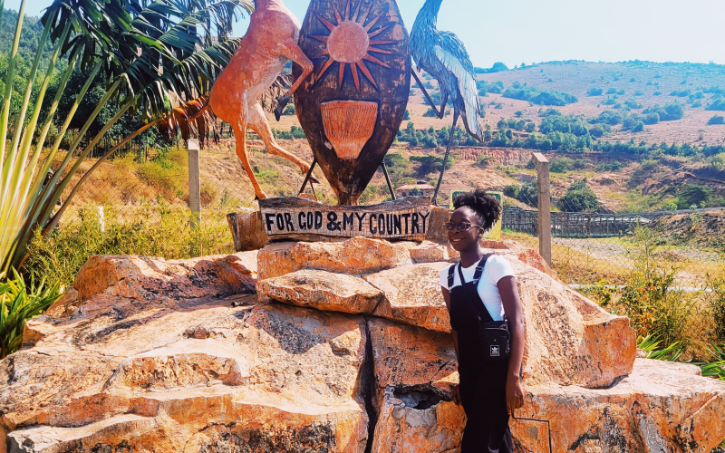 Zari Ward stands in Uganda next to the Ugandan coat of arms.