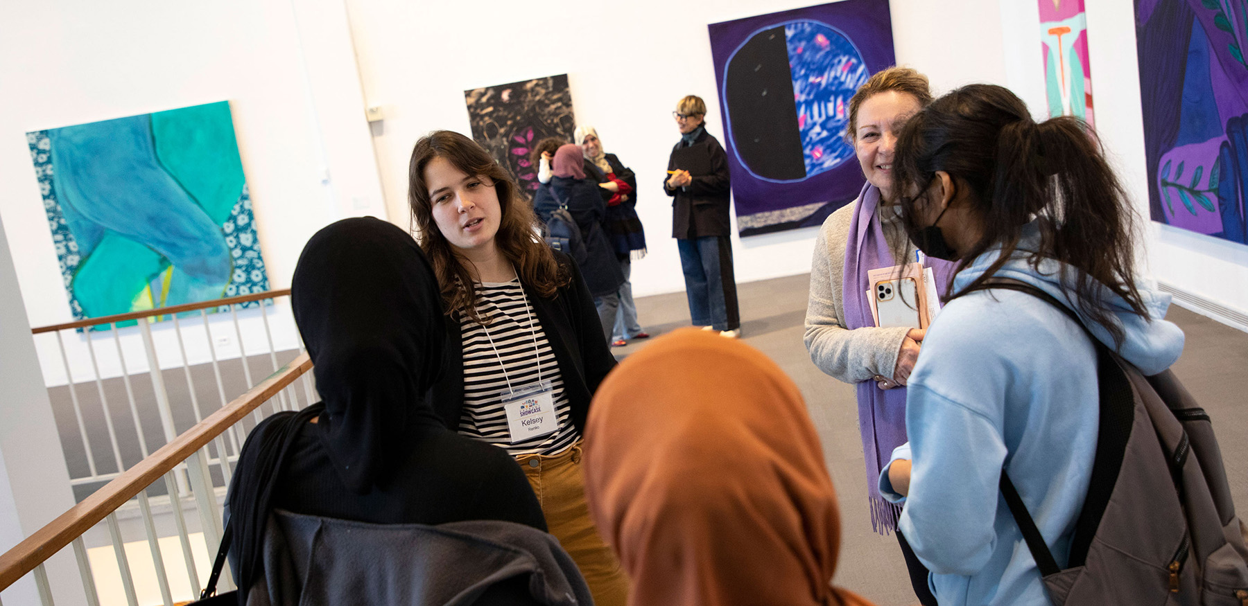 An artist speaks to a group of three students while a smiling professor looks on inside the University Art Museum..