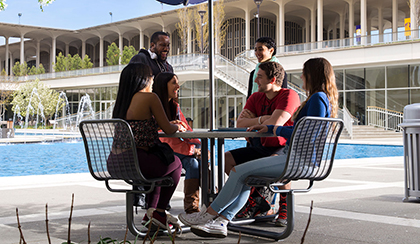A group of students sitting at a table by the fountain together. 