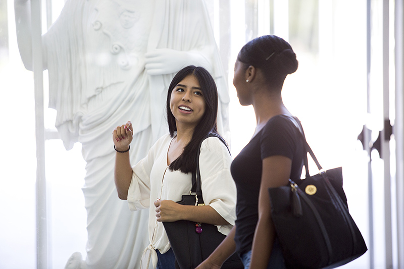 Two students walking near a statue of Minerva in the UAlbany Science Library.