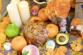 Fruit and bread are pictured atop a colorful table decorate with candles, marigolds and photos of lost loved ones.