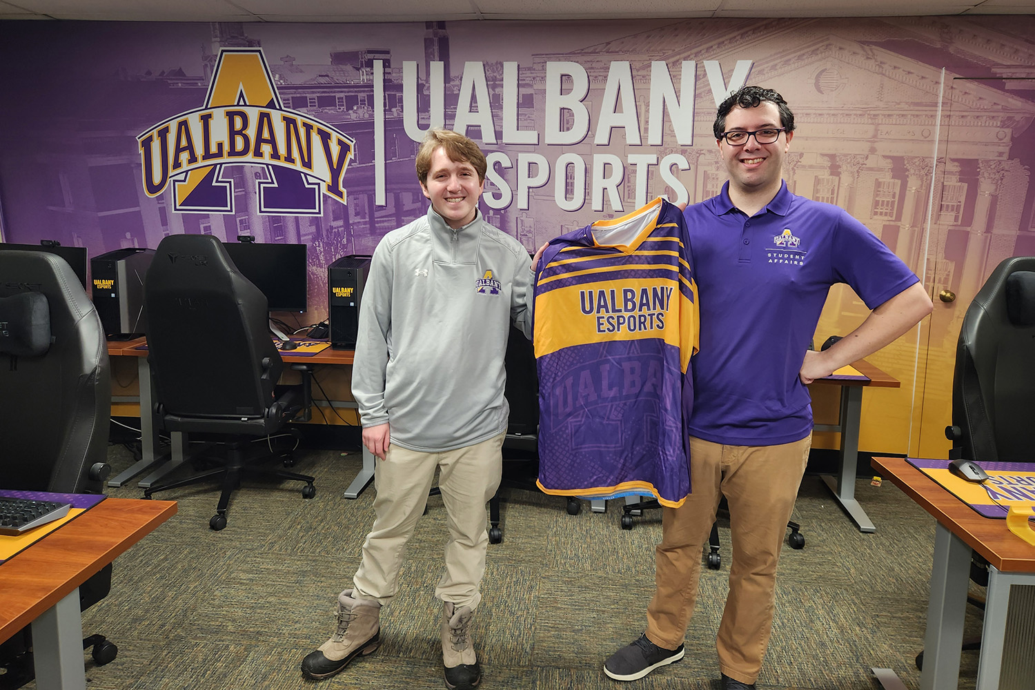 J.T. Stone and John Macone hold up a jersey inside the UAlbany Esports arena on the Downtown Campus.