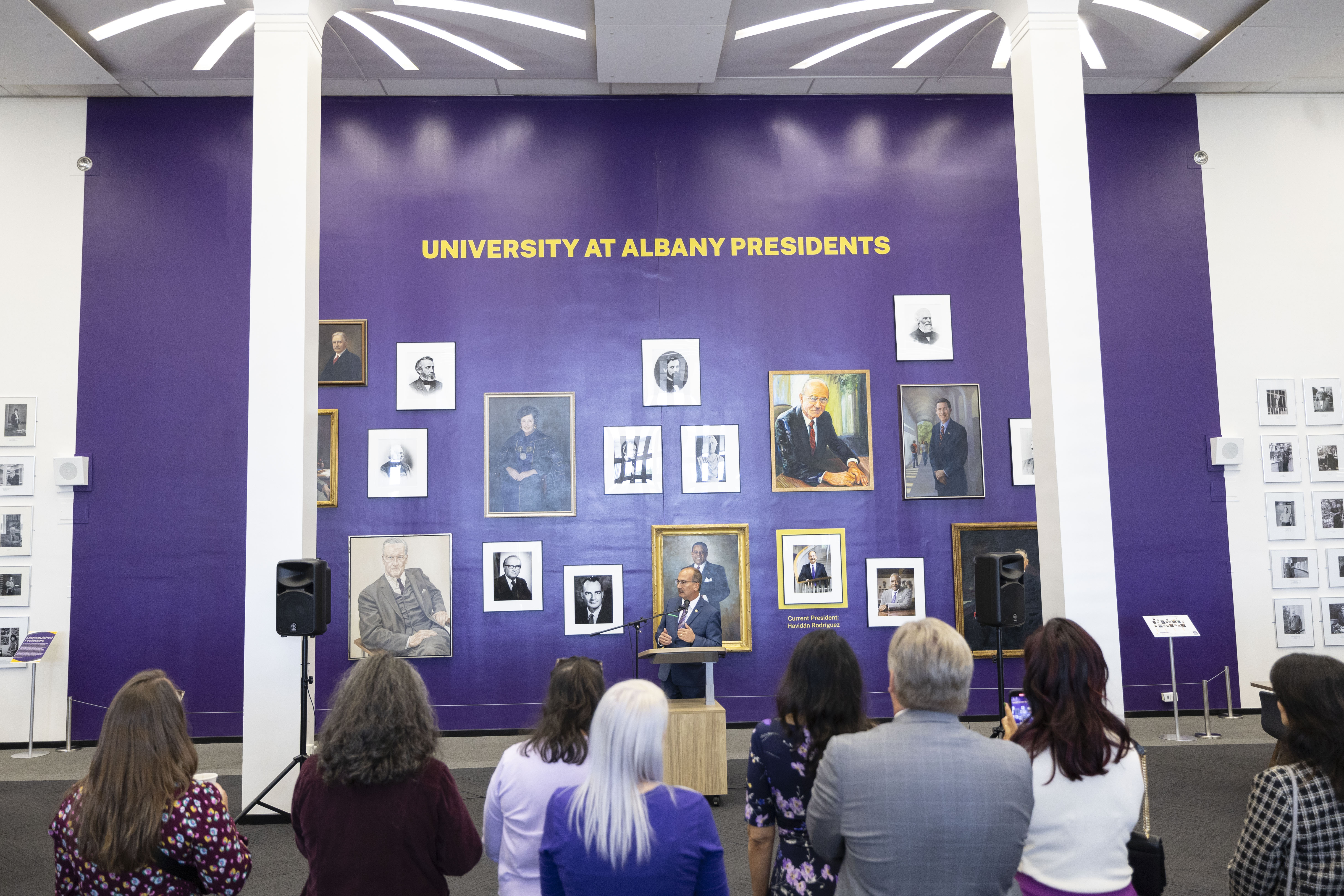 President Rodriguez at the podium in front of a portrait gallery of past University presidents