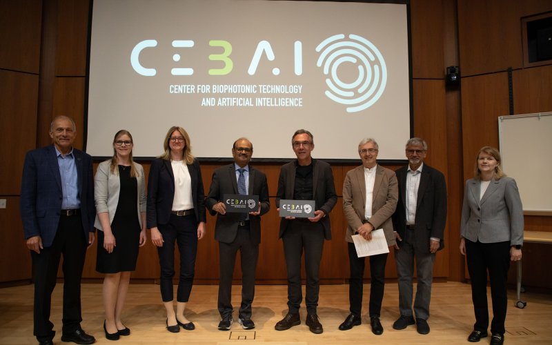 Leaders from UAlbany and the Leibniz Institute stand in front of a projection screen with the CEBAI logo on it.