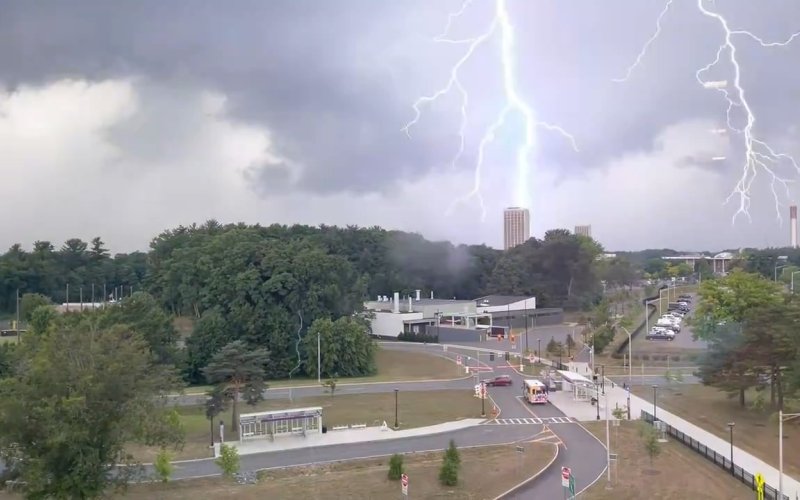 A scene of lightning striking a tall white tower in the medium distance, with roads and parking lots in the foreground.