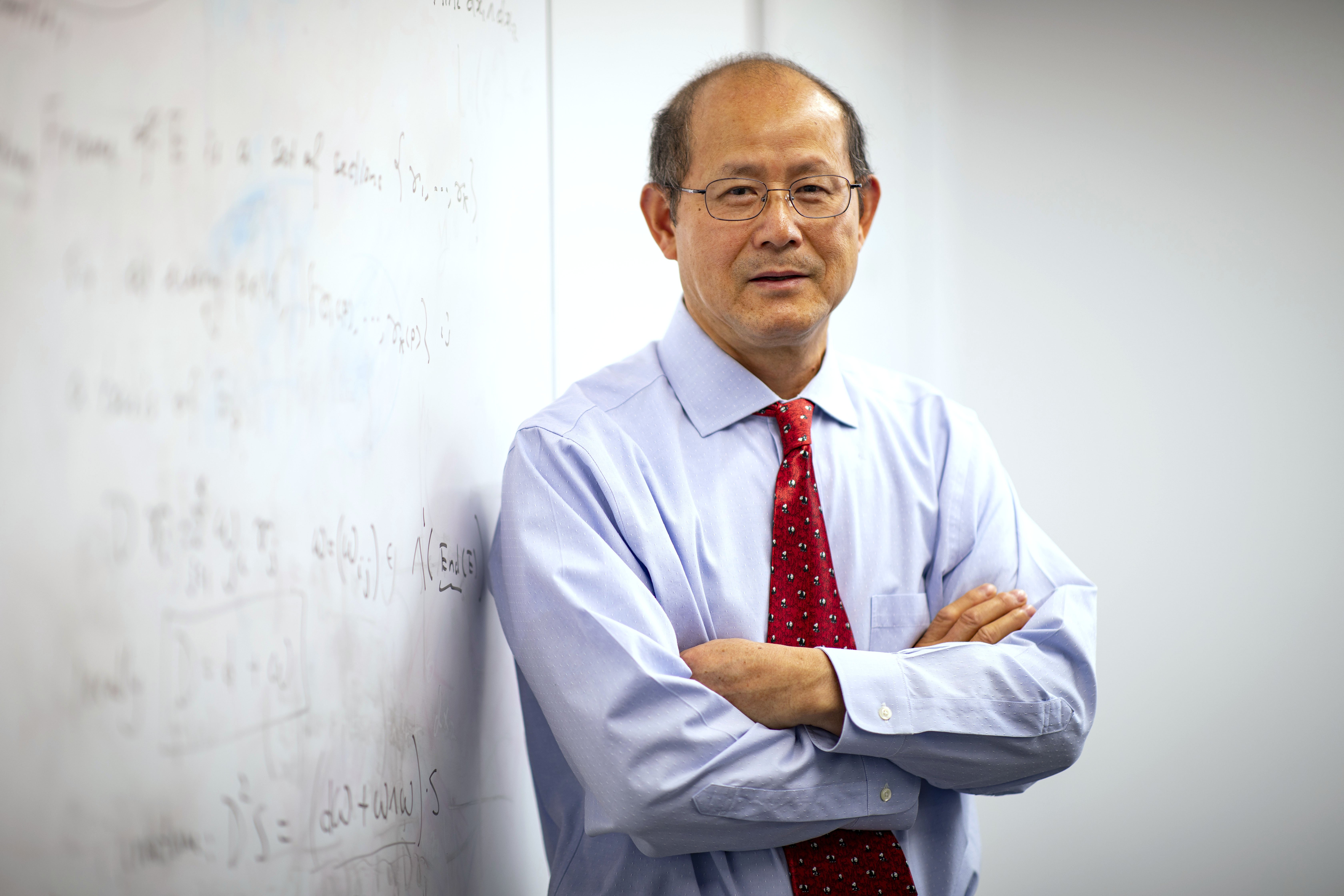 UAlbany Professor of Mathematics and Statsticis Kehe Zhu stands next to a white board.