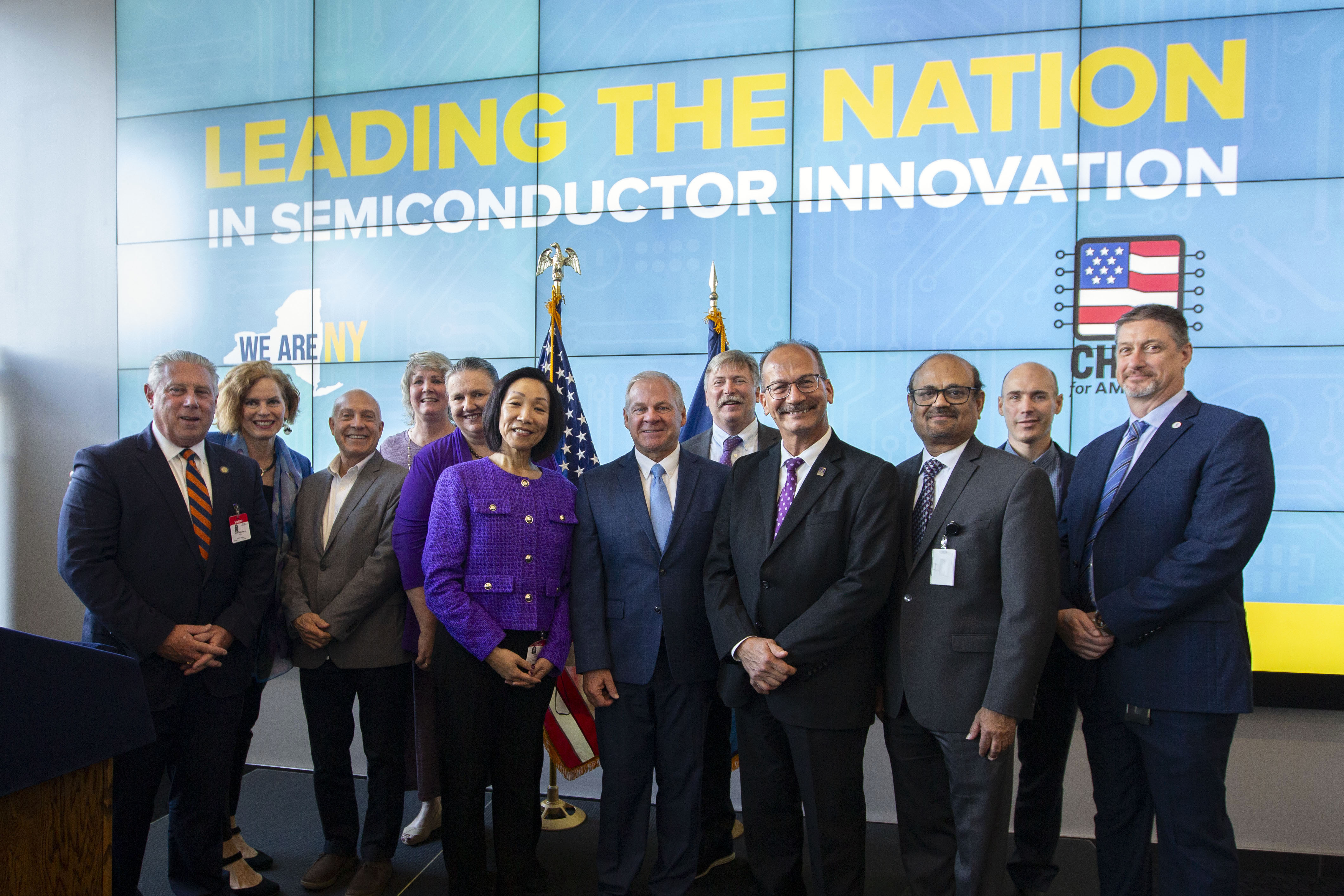 A group of people smiling toward the camera in front of a blue screen that reads: "Leading the Nation in Semiconductor Innovation."