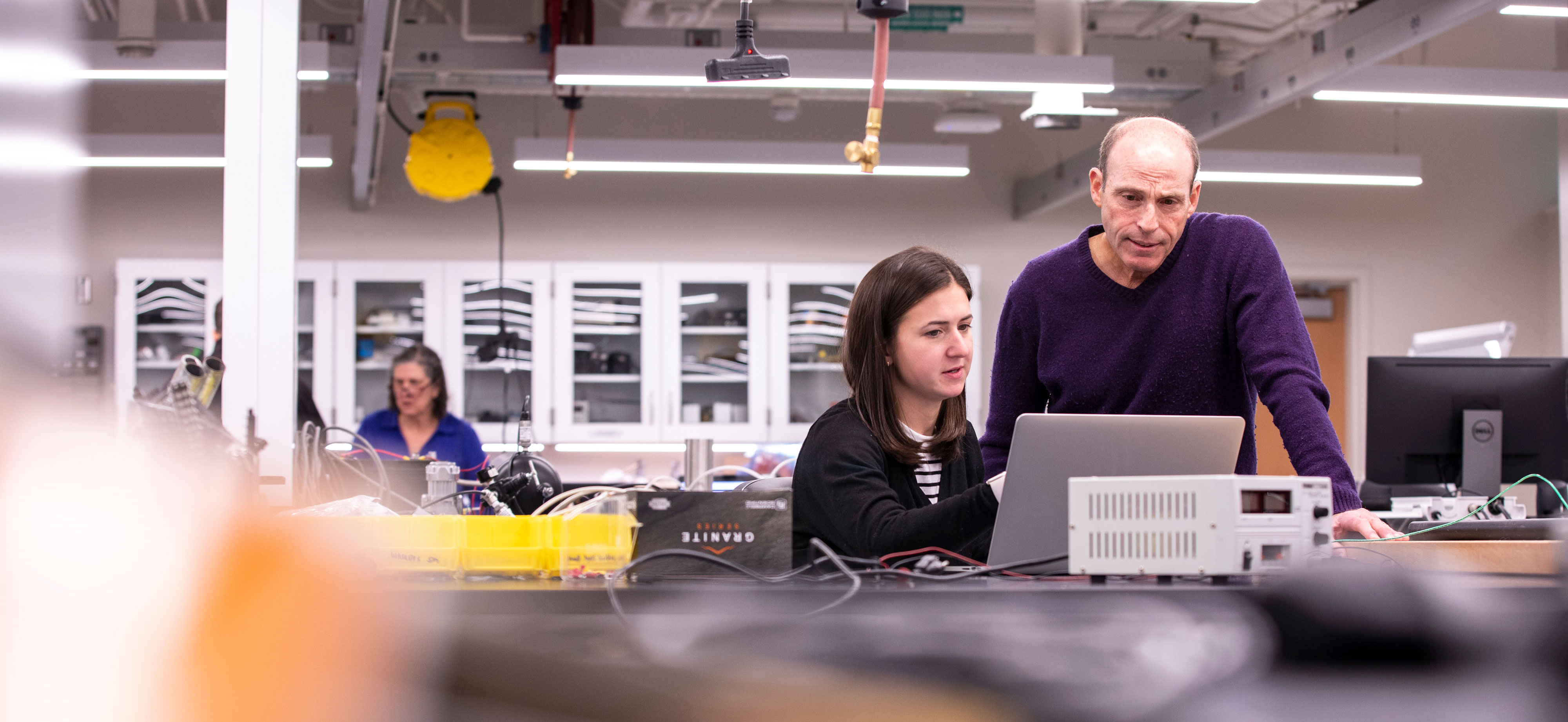 Two University employees, one who is seated and one who is standing, collaborate on a computer inside a lab.