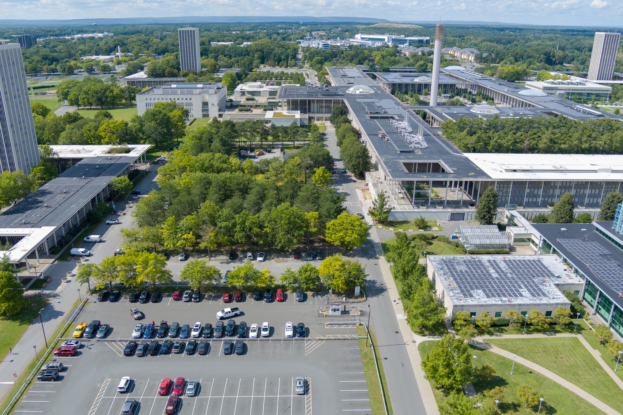 UAlbany's Uptown Campus, as photographed by a drone on a partly cloudy spring day. A parking lot, campus buildings and green trees are visible