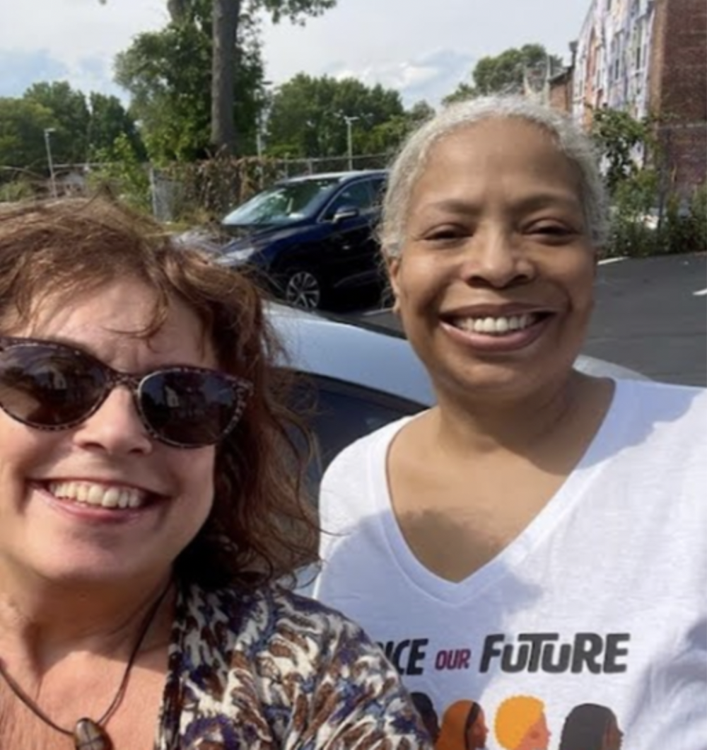 Two women smile for a selfie in a parking lot.