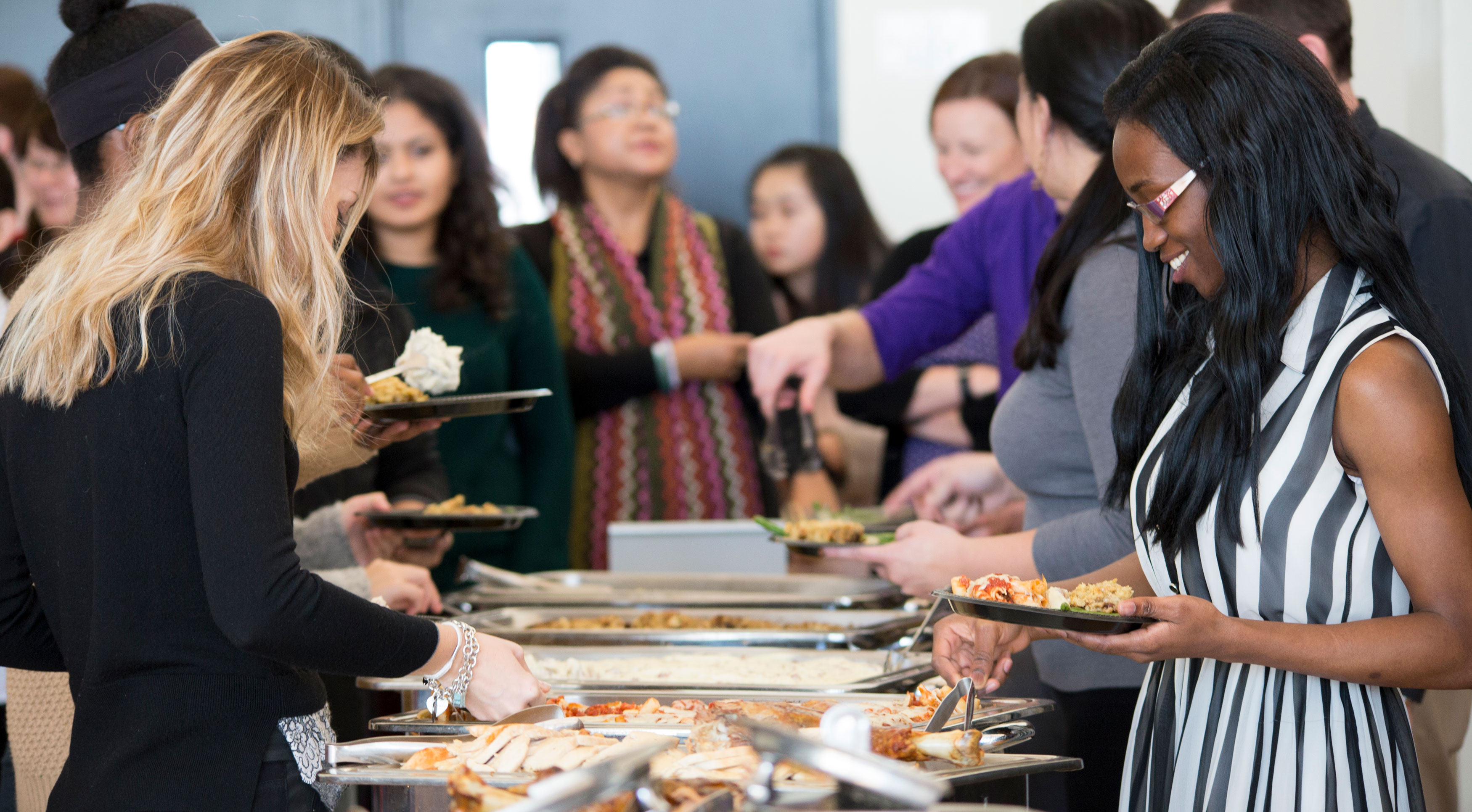 Attendees at a campus event smile as they serve themselves food from a buffet line.