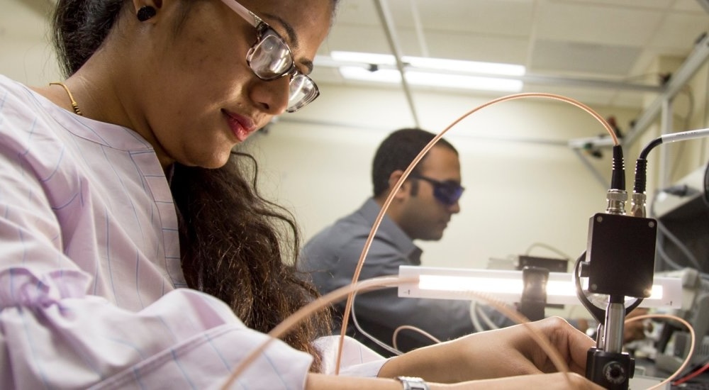 Researcher in foreground tests a piece of equipment in the Department of Electrical & Computer Engineering.