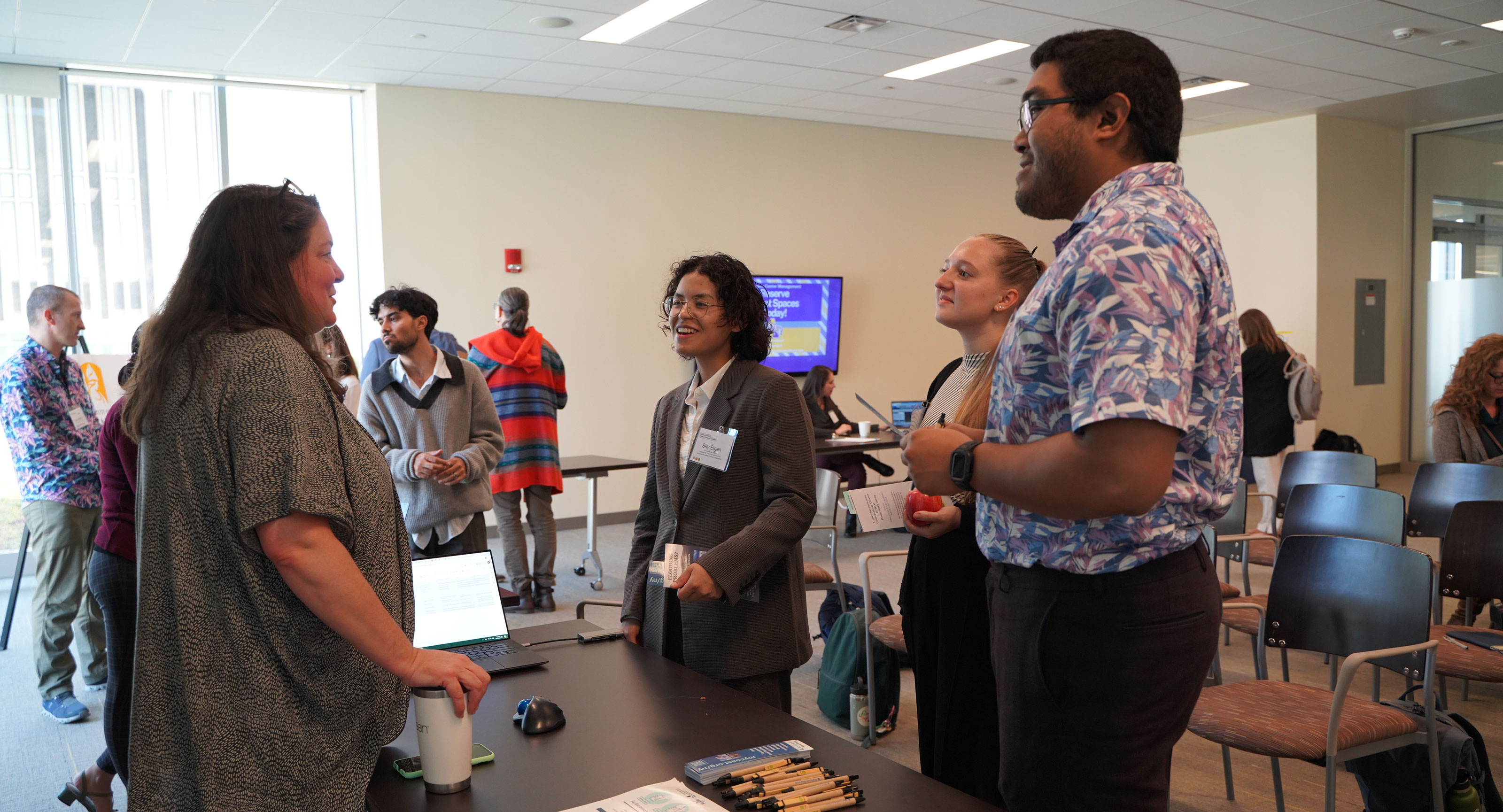 Three individuals smile and nod as they speak to a fourth individual at a tabling event.