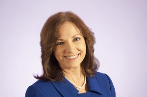 A portrait of a woman with brown hair wearing a blue dress, smiling toward the camera.