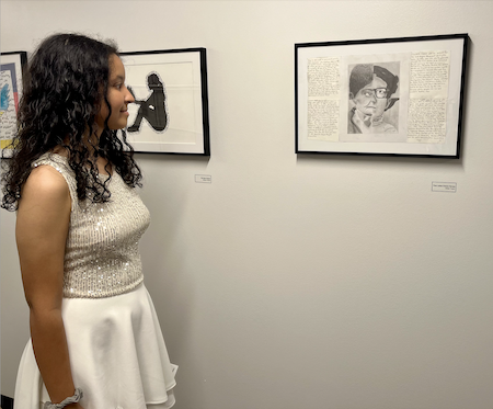 A teenage girl with long curly black hair wears a white skirt and top and stares at a portrait she drew of civil rights activists hanging in a hallway.