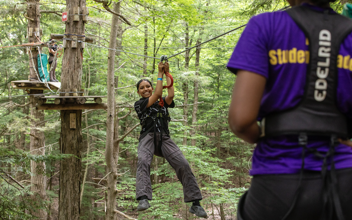 A young person hangs from a high ropes course in the middle of a forest.