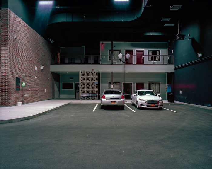 Two cars sit in a parking lot in front of what appears to be a motel but is actually a site used to train security personnel for emergencies and disasters.