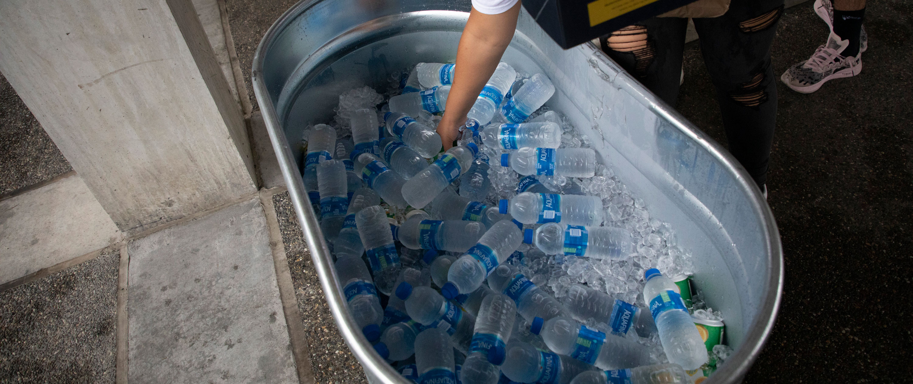 A hand reaches into an aluminum tub filled with ice and water bottles.