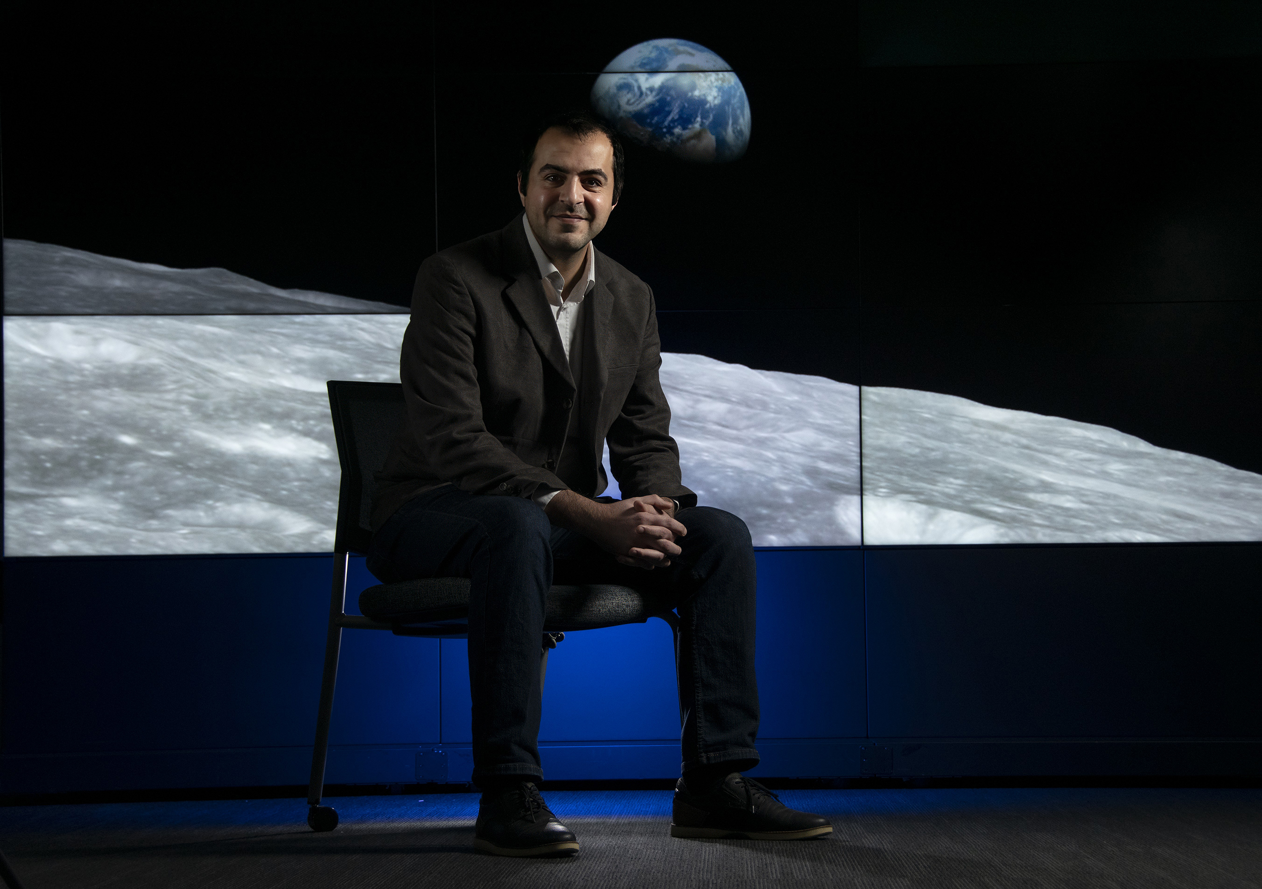 UAlbany researcher Mustafa Aksoy sits in front of a multi-screen display of a NASA image the Earth rising over the horizon of the moon.