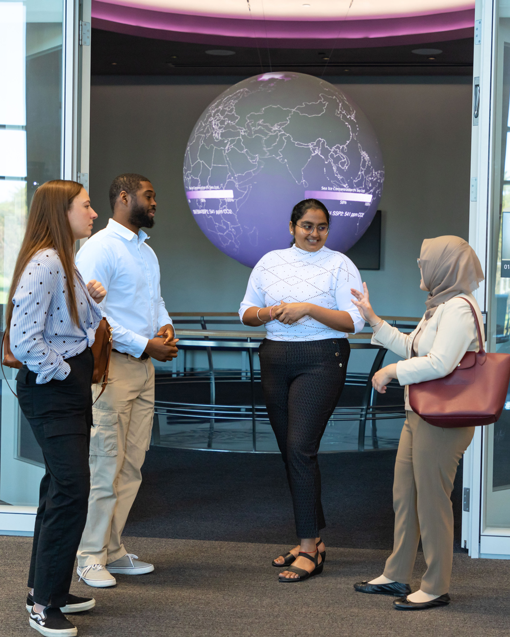 Four students having a discussion in front of a globe in UAlbany's ETEC building.