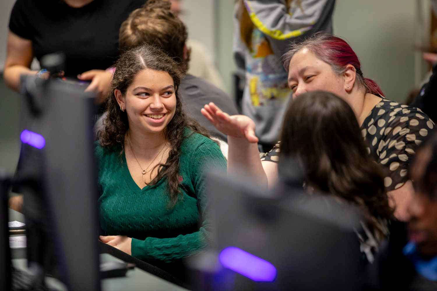 Students and a professor having a discussion in front of large computer monitors.