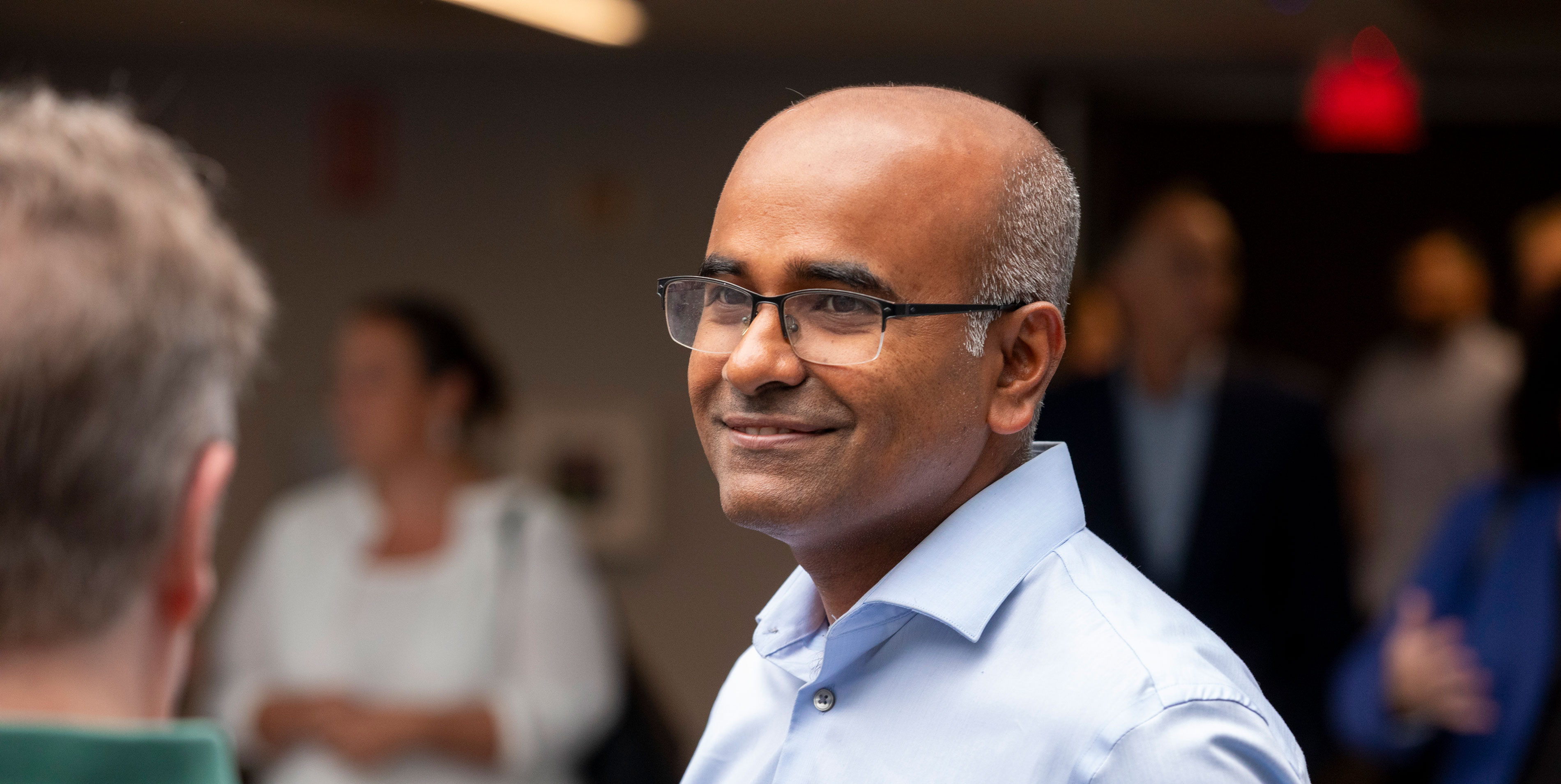 A University employee smiles while speaking to another person.