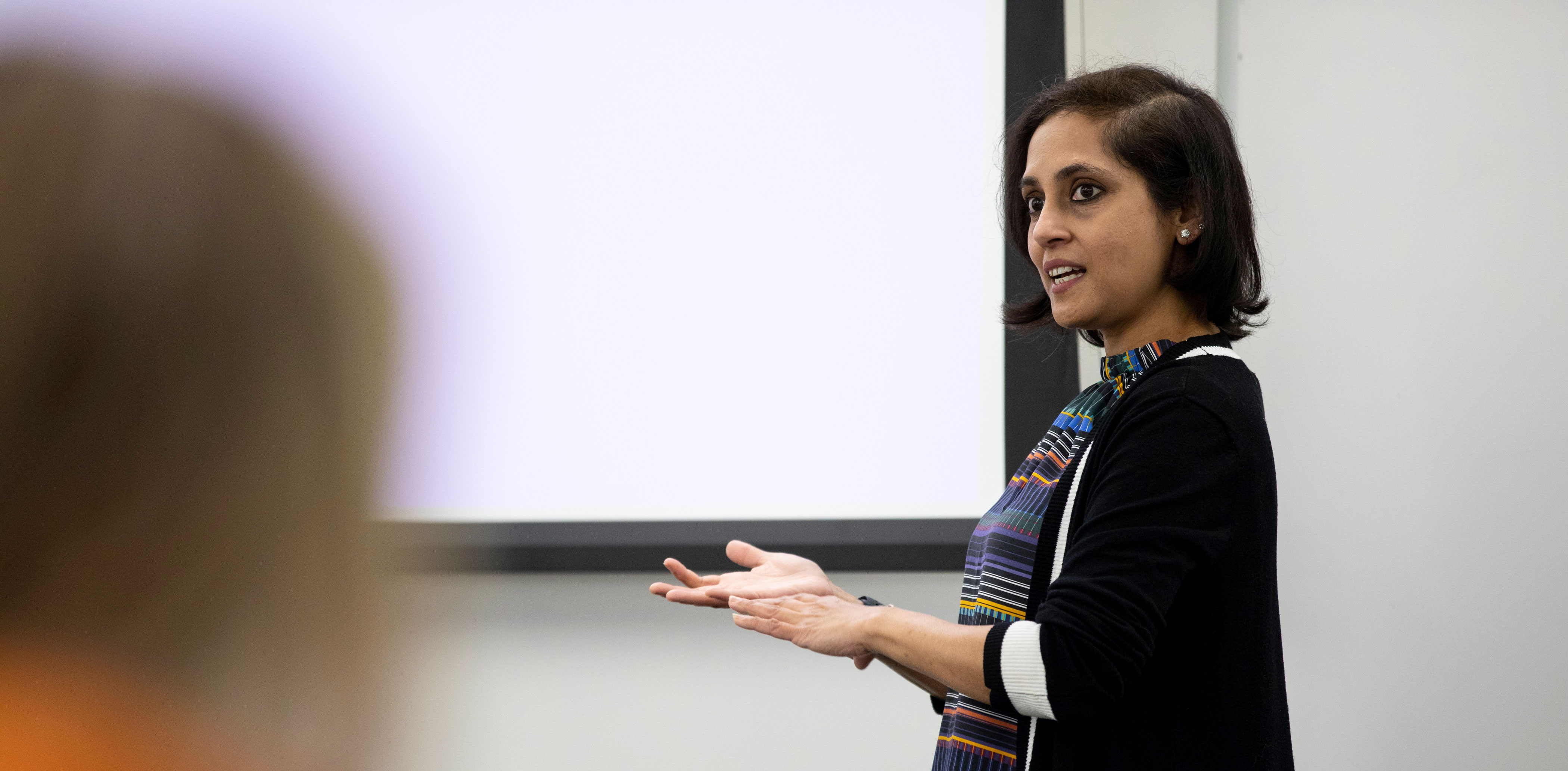 A faculty member gestures while speaking in front of a classroom full of students.