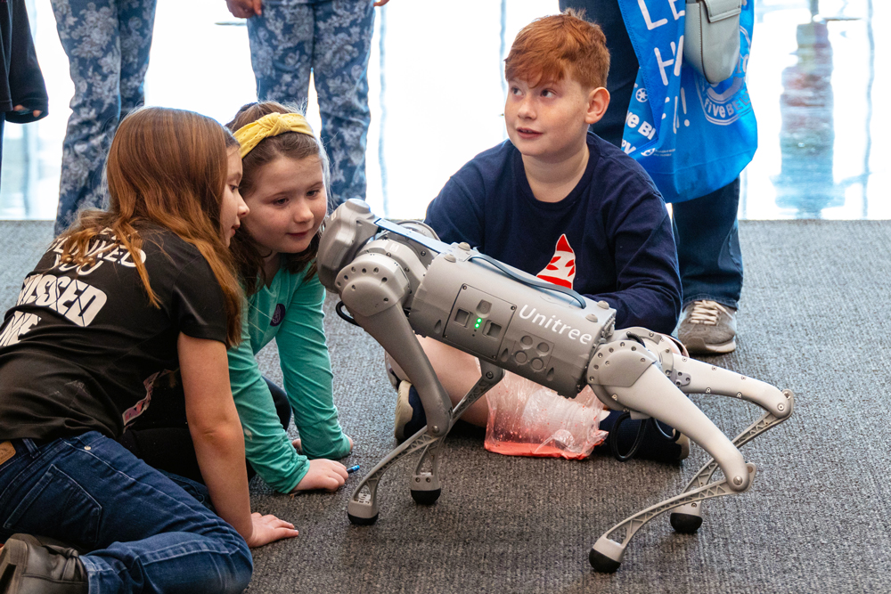 Three children interacting with a robot dog at UAlbany STEM and Nanotechnology Family Day.