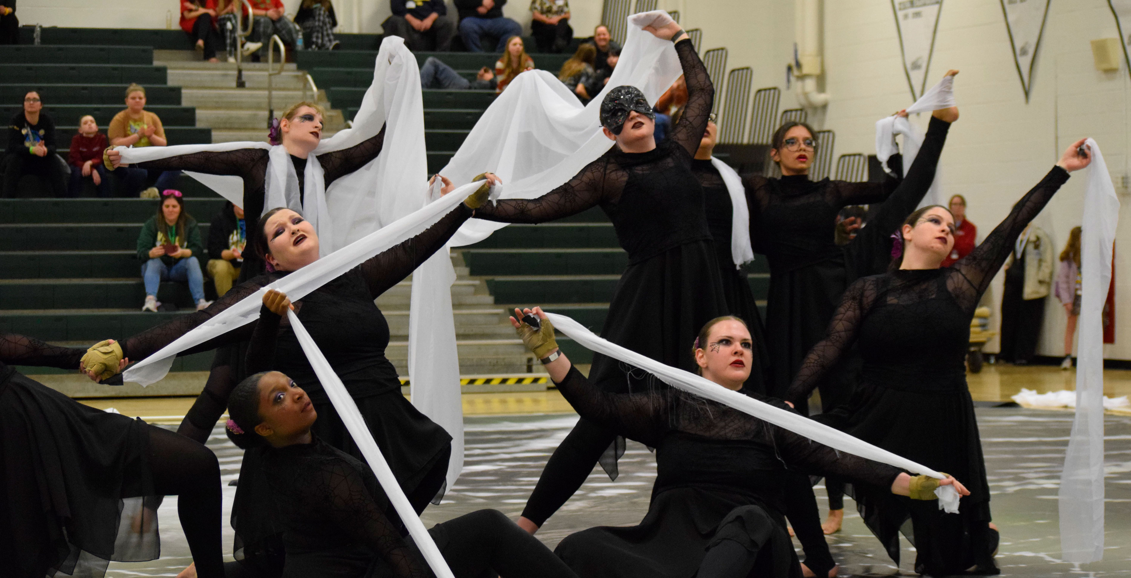 The UAlbany Winter Guard performs with all black costumes and lengths of white fabric inside a gymnasium.