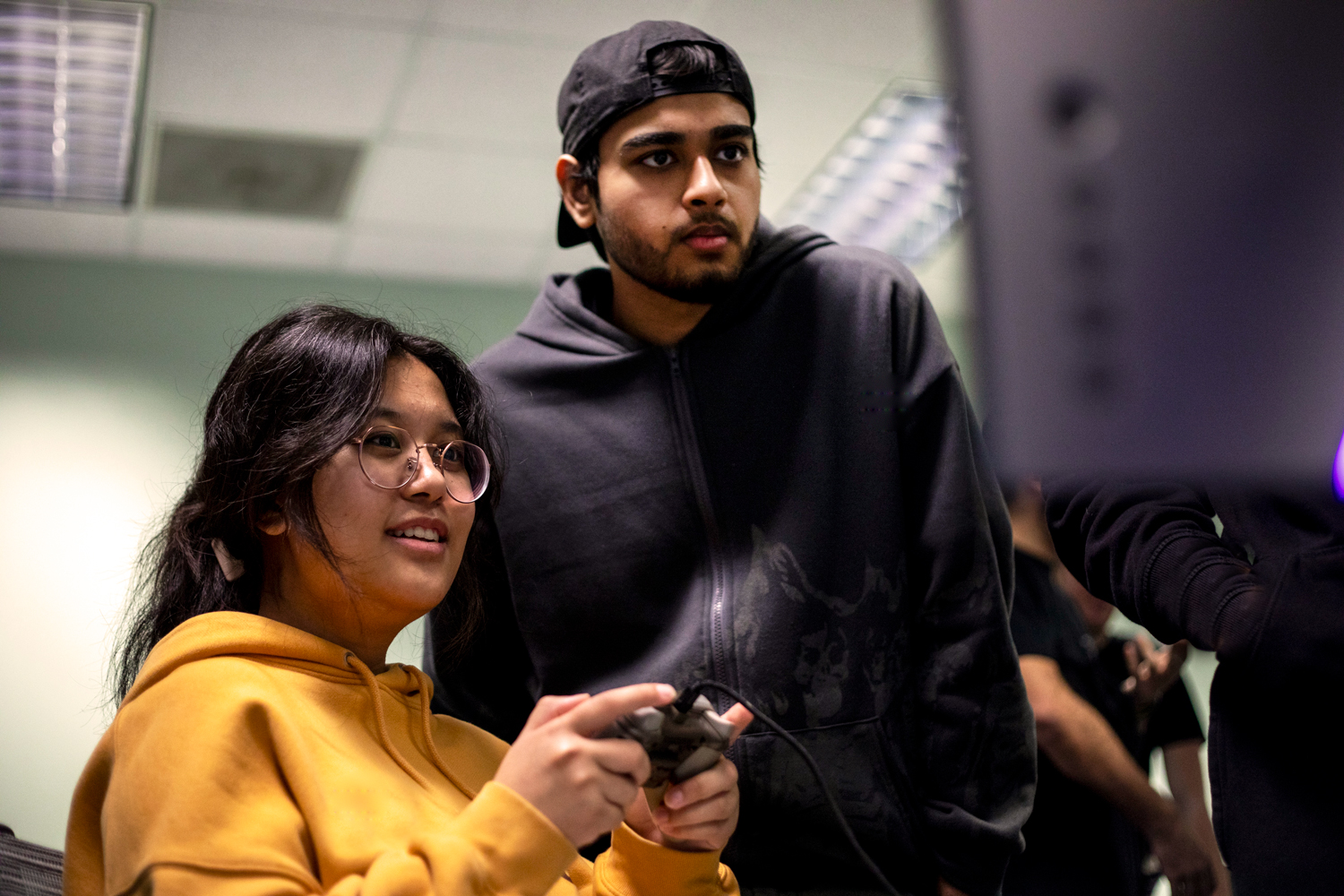 A student holds a gaming controller while another looks on at the monitor.