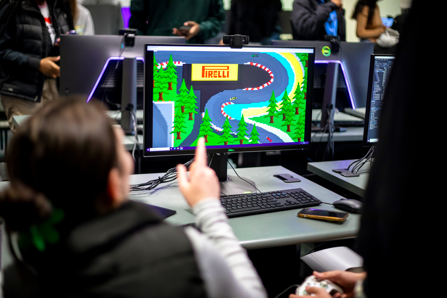 Students looking at a video game on a computer monitor while holding a game controller.