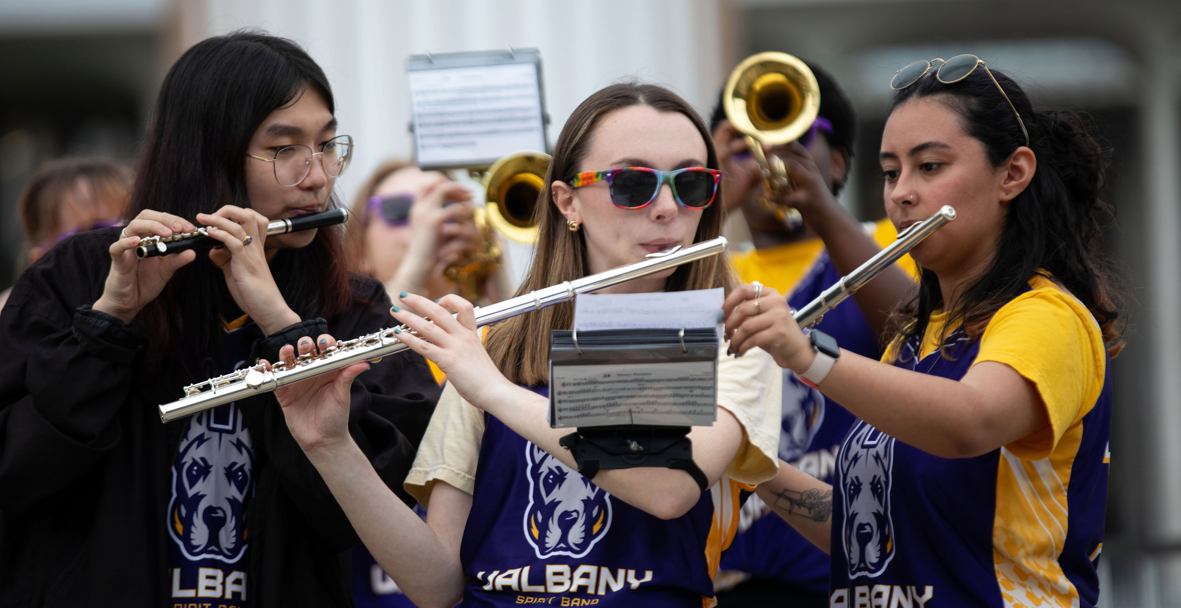 Three students from the UAlbany Spirit Band play woodwinds during an outdoor performance.