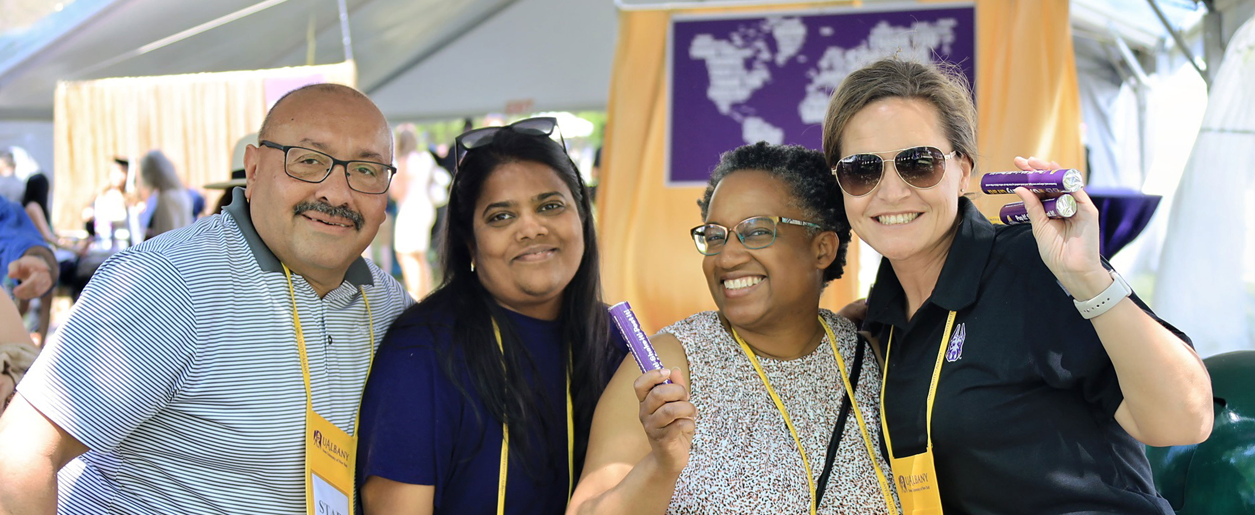 Four UAlbany faculty and staff members smile and pose at a Commencement event.