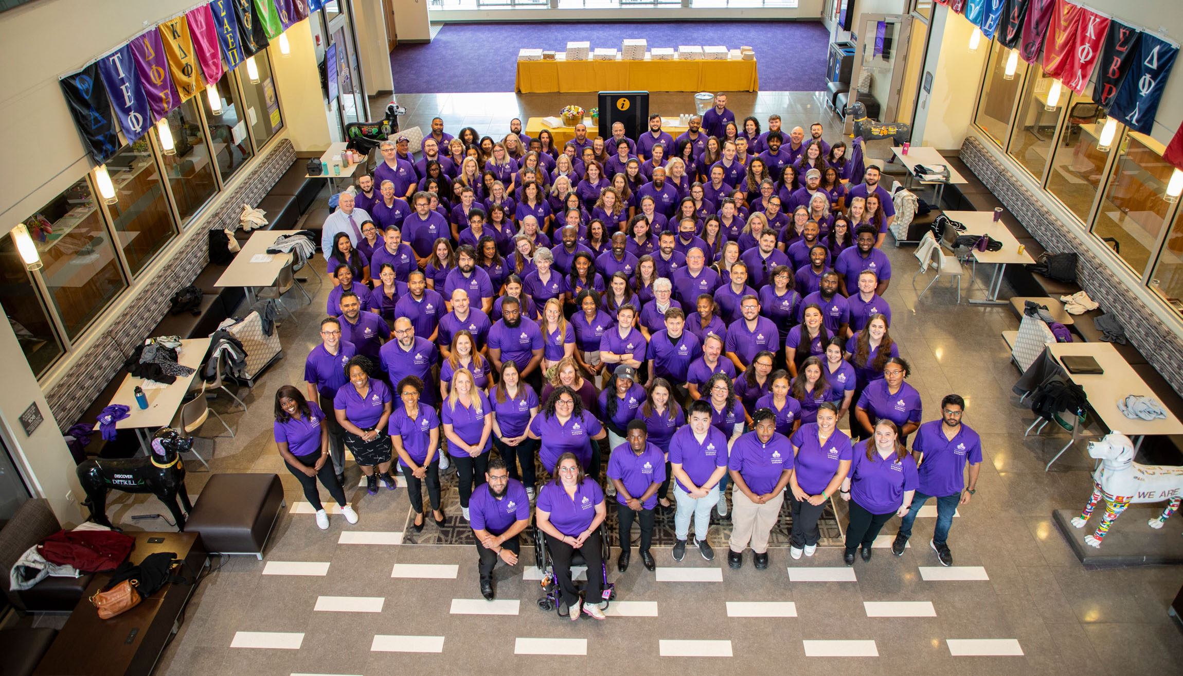 Dozens of employees from the Division of Student Affairs & Enrollment wearing purple polo shirts pose for a group photo inside UAlbany's Campus Center.