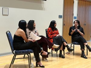 Four panelists sit and speak at the front of an auditorium during a conversation and Q&A featuring authors Angie Cruz and Lilliam Rivera.