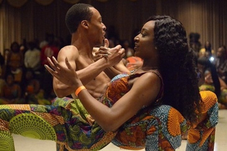 Two African American dancers wearing traditional garb perform on stage.