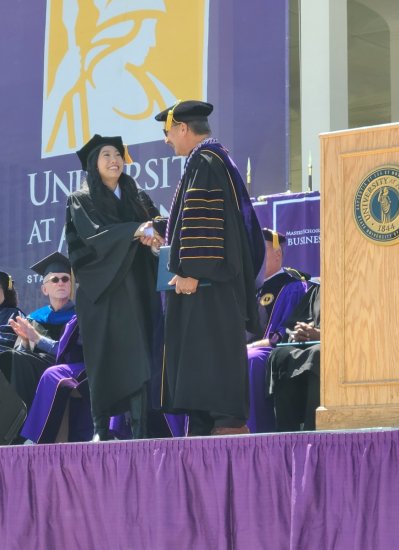 Nora Lum shakes the hand of UAlbany President Havidán Rodríguez as she receives her honorary doctorate at UAlbany's commencement ceremony.