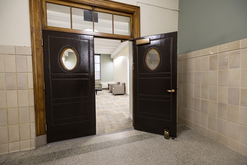 A photo of two large brown leather doors, one of them open, that lead to a new office space.