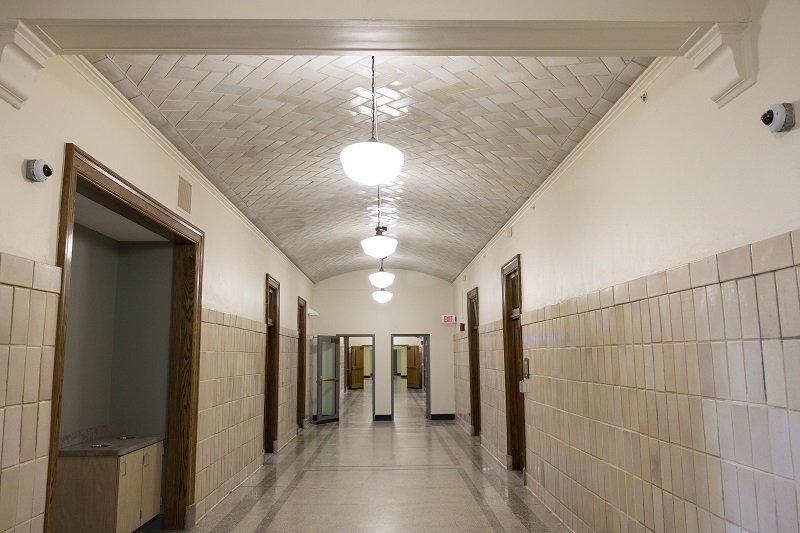 A photo of a long empty corridor with historic tile ceilings and original woodwork around the doors.