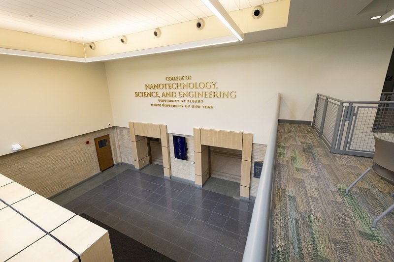 An empty, two-story lobby photographed from the second-floor balcony. The words "College of Nanotechnology, Science, and Engineering" are on the wall.