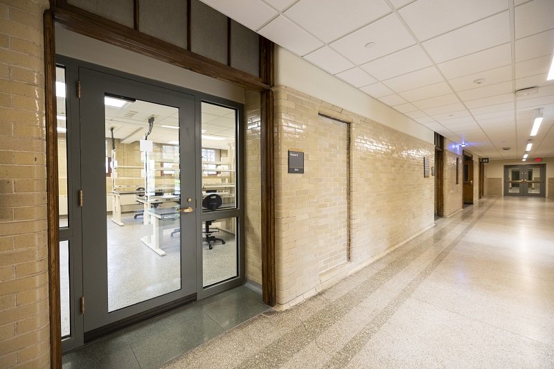 A brightly lit modern lab photographed from a long, brick hallway through a glass door.