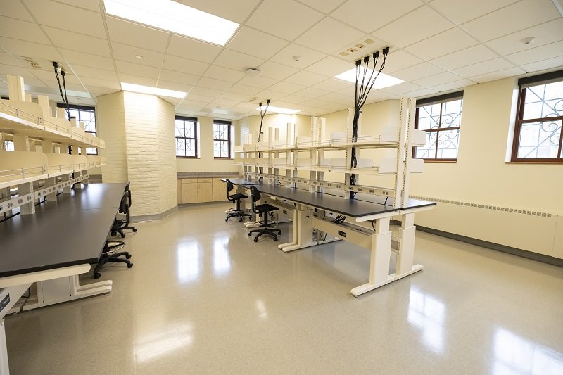 An empty lab space in which modern lab benches are set up next to century-old white brick walls.
