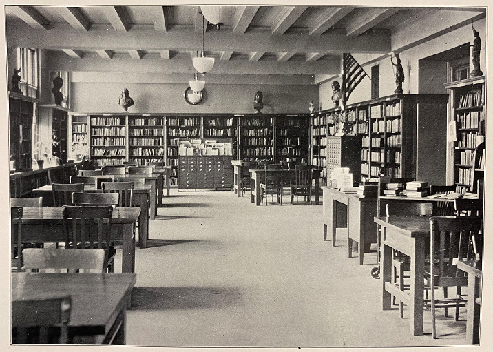 A black and white photo of a library with several tables and walls lined with bookshelves.