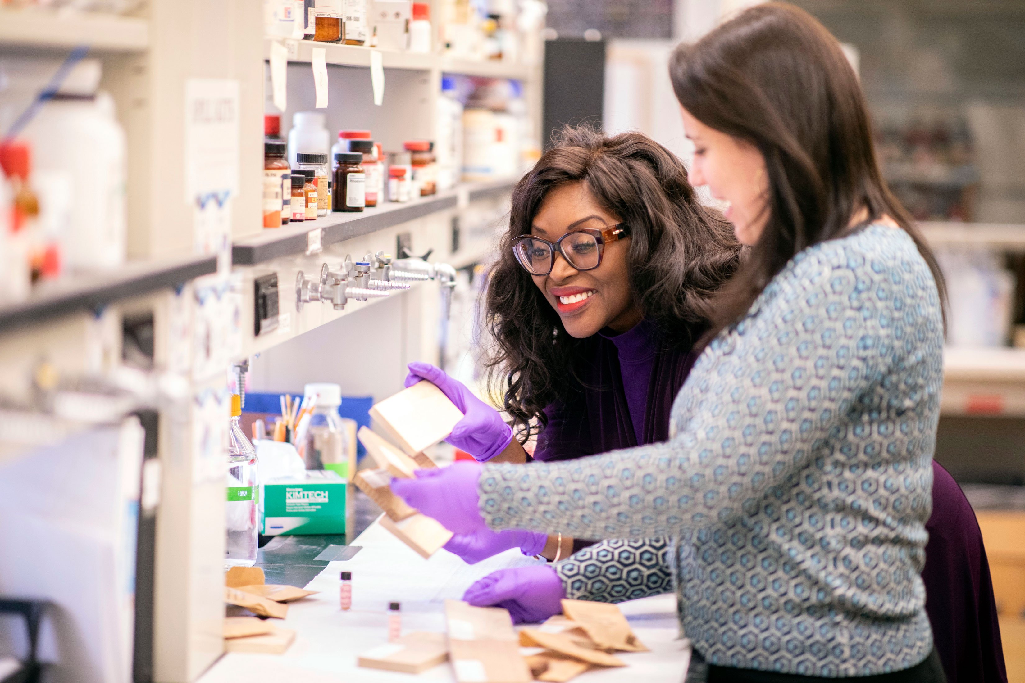 A faculty member smiles as she leans over and collaborates with a student employee inside a chemistry lab.