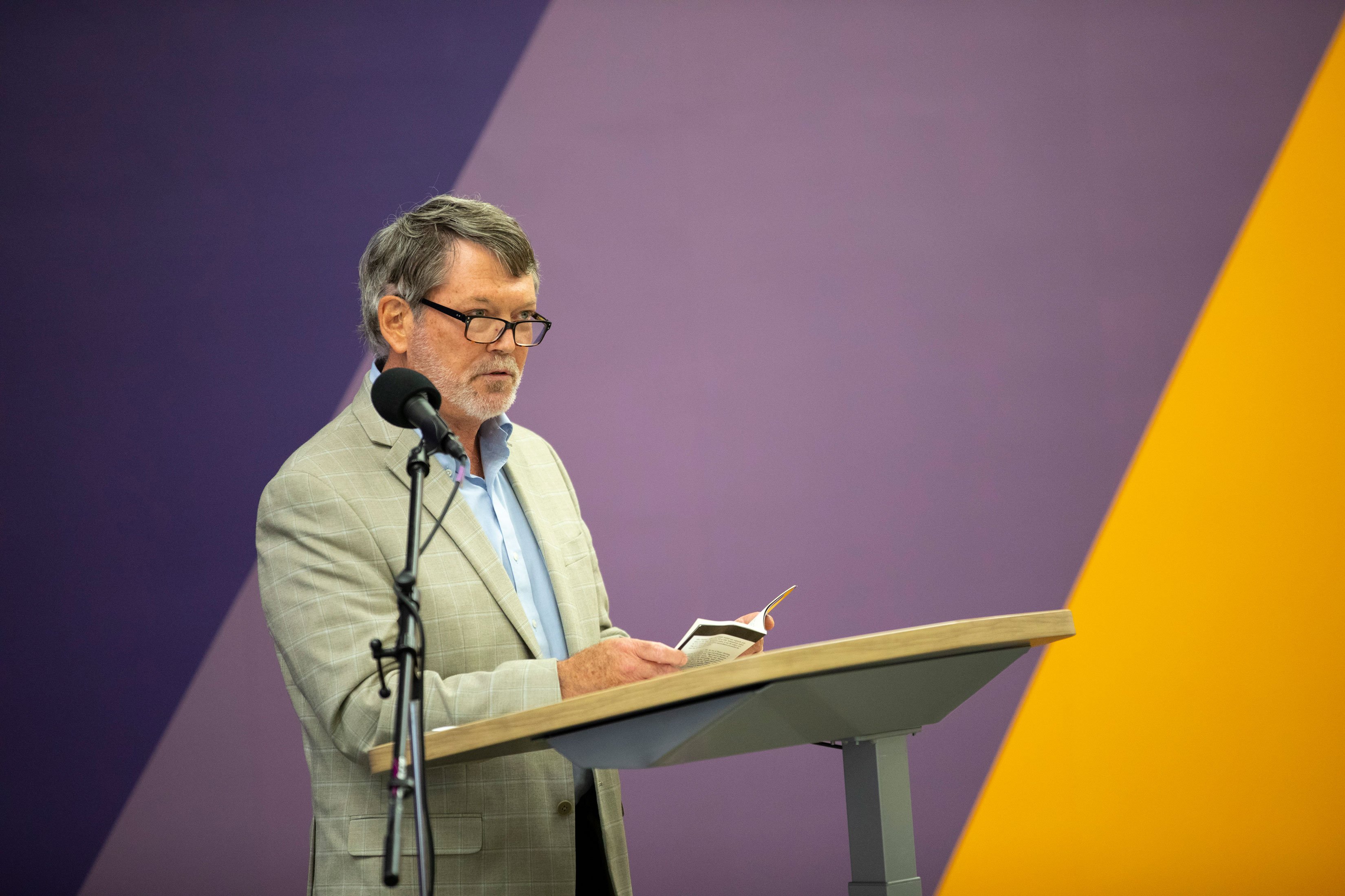 A faculty member reads from a paper while standing at a podium.